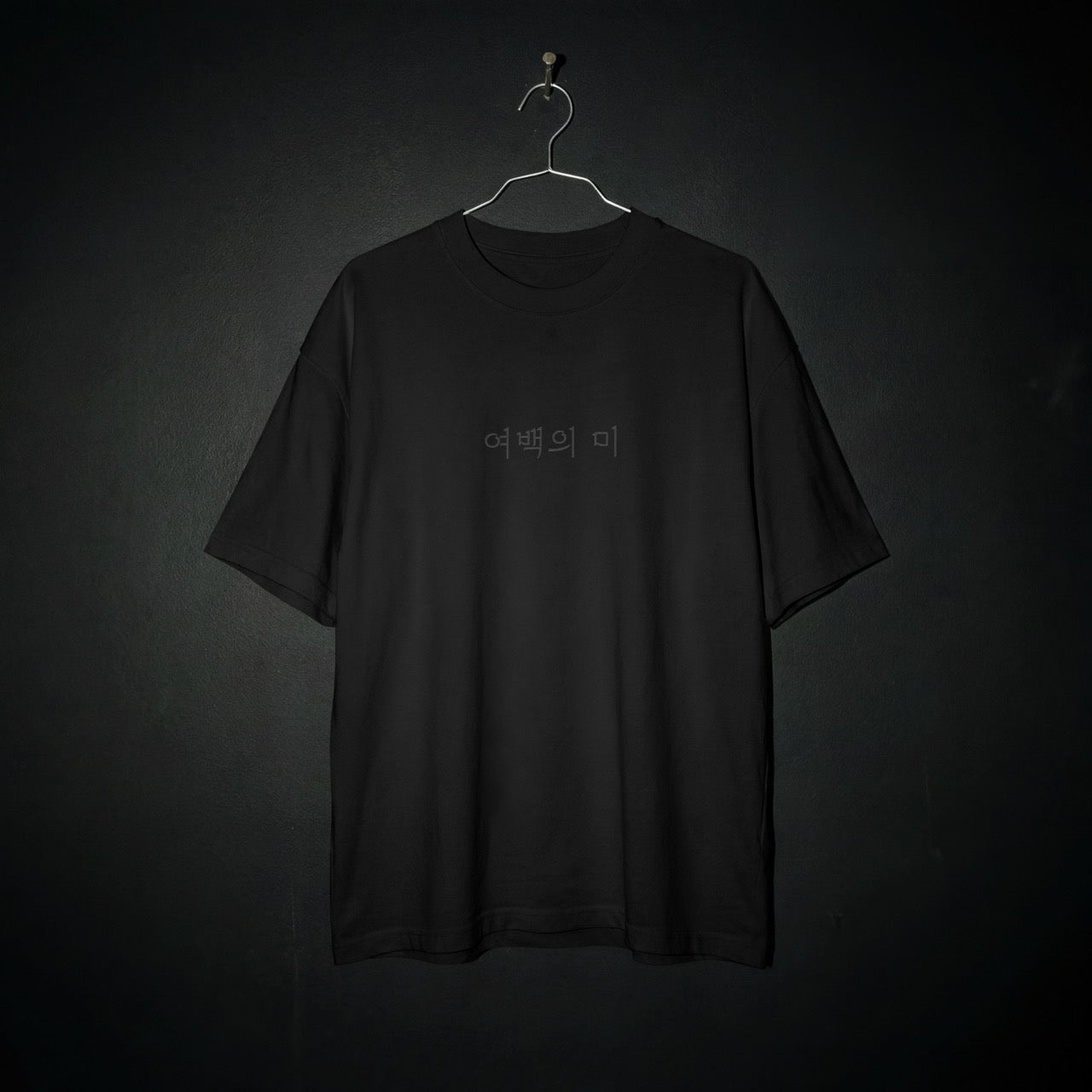 Nuqta heavyweight black T-shirt on hanger featuring minimalist black-on-black Korean typography. UK Brutalist streetwear.